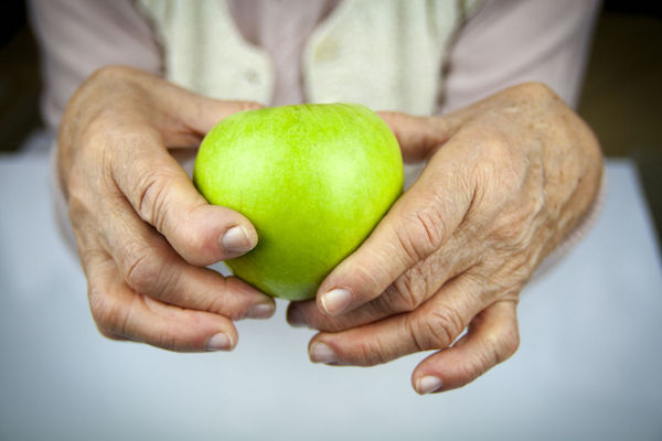 An elderly person holding an apple