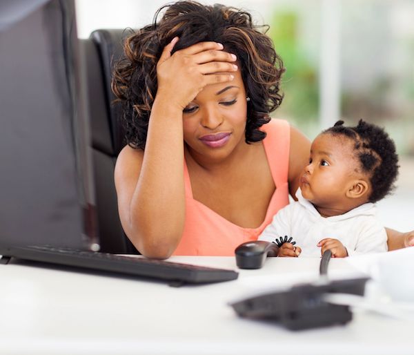 Postnatal depression A woman holding her head at her desk with her baby